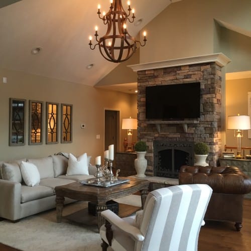 In the living room, the oversized sofa is replaced with a silvery three seater, and the stone fireplace is still an intricate design focus.
