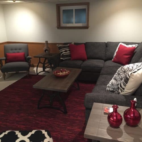 The Eads basement family room uses red as a pop of color paired with bold patterns on pillows and other smaller accessories against a great neutral base of black and gray